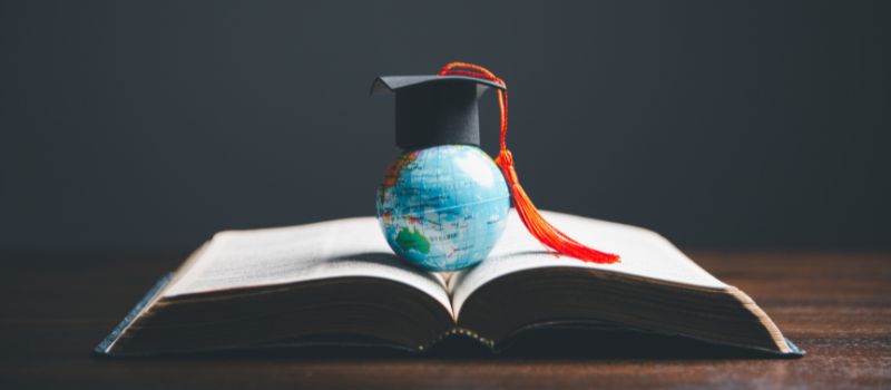 A miniature globe with a graduation cap on top placed on an open book.
