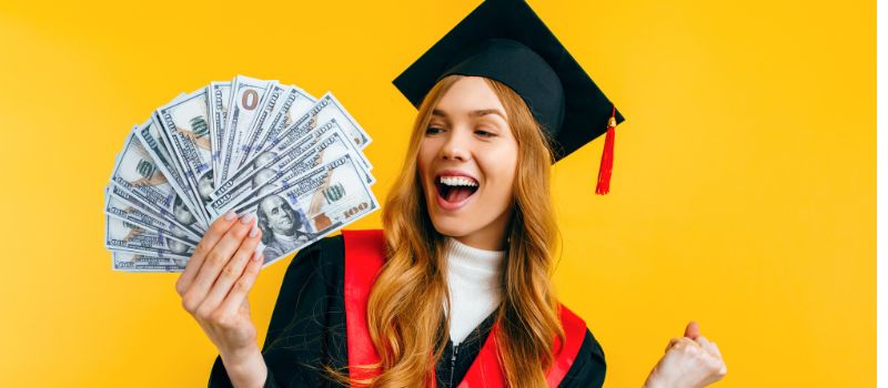 Person in a graduation cap and gown holding a fan of cash against a yellow background.
